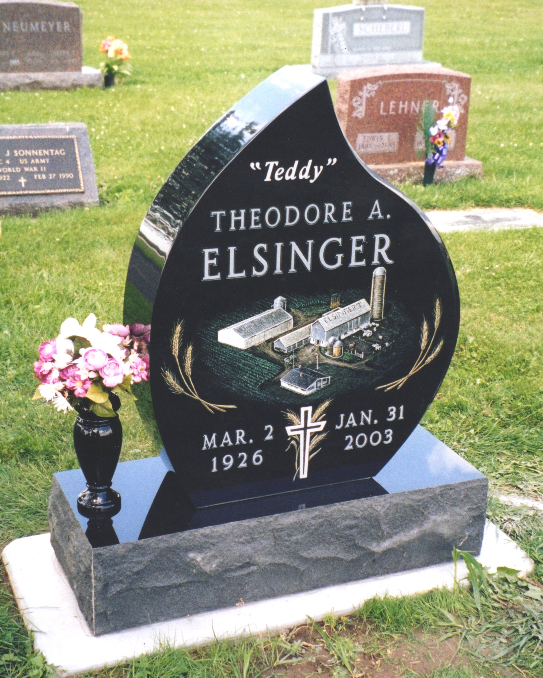 A black granite tombstone with gold lettering and a vase of flowers.