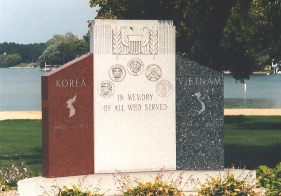 A monument in the middle of a park with trees and bushes.